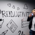 Productivity - man holding smartphone looking at productivity wall decor
