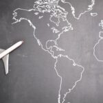 Global Business - Top view of miniature airplane placed on over gray world map with crop hand of anonymous person indicating direction representing travel concept
